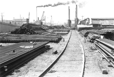 Rail unloading & storage yard; rolling mill in the background.